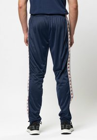 Marine sportbroek met elastische tailleband, zijkant met witte en oranje logo-streep, taps toelopende pasvorm, gemaakt van gladde, lichte stof.