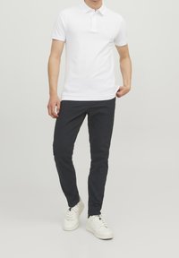Vit pikétröja med krage, korta ärmar och diskret logotypdetalj, tillsammans med marinblå slim fit-byxor och vita sneakers.