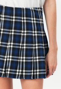 Blauw en zwart geruite plooienrok met witte accenten, gemaakt van een gestructureerde stof en een tailleband bovenaan zonder zichtbare sluitingen.