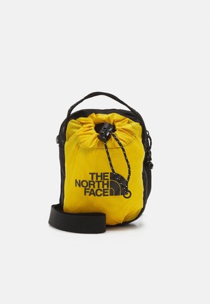 Mała czarno-żółta torba na sznurki North Face z paskiem na ramię i logo na przodzie na białym tle.