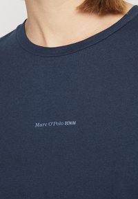 Sötétkék, rövid ujjú pamut póló, kerek nyakkivágással, a mellrészen kis fehér szöveglogóval: "Marc O'Polo DENIM".