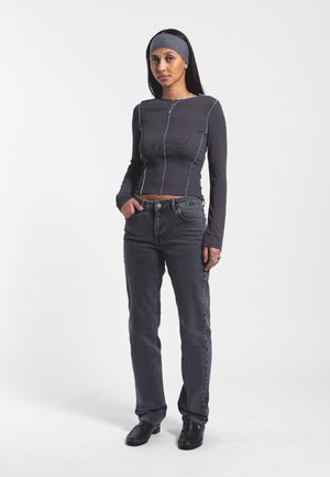 Langærmet, ribbet top i mørkegrå med blå sømme; parret med højtaljede mørkeblå jeans og sorte slip-on sko.