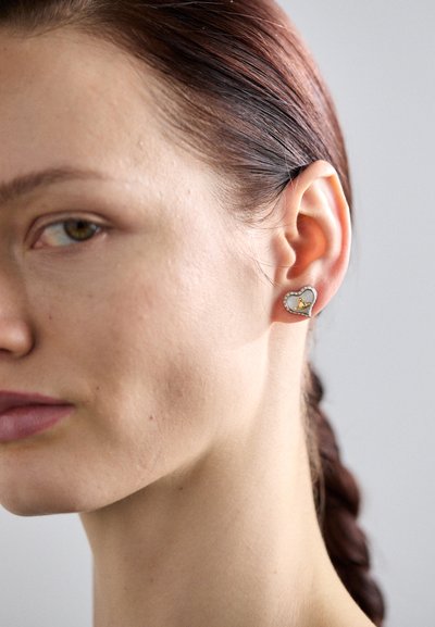 Orecchini a forma di cuore in argento presentano un sottile contorno con un piccolo cuore dorato all'interno, accentuato da piccole pietre brillanti.