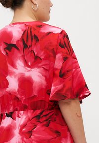 Vestido florido vermelho com mangas curtas em babados, apresentando um padrão abstrato vibrante em tons de vermelho e rosa. Tecido suave com cintura elástica.