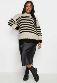 Kofta i stickad med krämfärgade och mörkgröna ränder, kombinerad med en svart satinmediklänning och svarta snörda kängor.