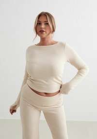 Beige ribbad långärmad topp i kombination med matchande högmidjade byxor. Båda plaggen har en figurnära design och mjuk textur.