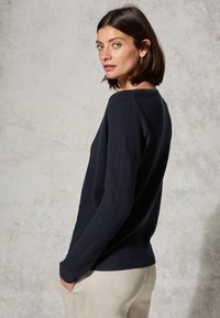 Marineblaues geripptes Sweatshirt mit langen Ärmeln und rundem Ausschnitt. Schmaler Schnitt, weich im Griff und minimalistisches Design. Kombiniert mit hellen Hosen.