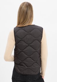 Dunkel gesteppte Pufferweste mit Wellenmuster. Sie besteht aus leichtem Material, hat ein ärmelloses Design und einen abgerundeten unteren Saum.