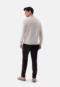 Maglione beige con polsini e orlo a costine, abbinato a pantaloni in velluto a coste scuri. Le scarpe dai toni neutri completano il look. Vista completa da dietro.