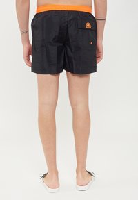 Pantaloni da bagno neri con un elastico arancione in vita, dotati di una tasca posteriore e un dettaglio di branding, realizzati in materiale leggero e a asciugatura rapida.
