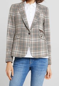 Blazer de cuadros en beige claro con patrones marrones y negros, con cierre de un solo botón, dos bolsillos frontales y un ajuste entallado.