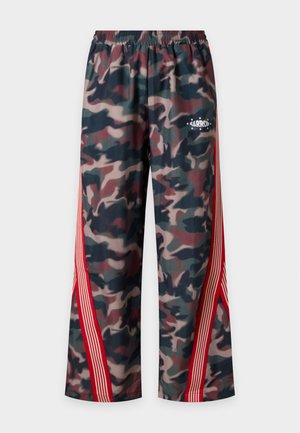 Homme portant un sweat à capuche vert foncé avec le texte "Keep Going" et un pantalon camouflage ample avec des rayures rouges, debout sur fond blanc.