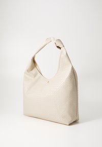 Sac à main tissé beige avec une forme hobo prononcée, une anse torsadée, une texture lisse et un petit détail en métal doré à l'avant.