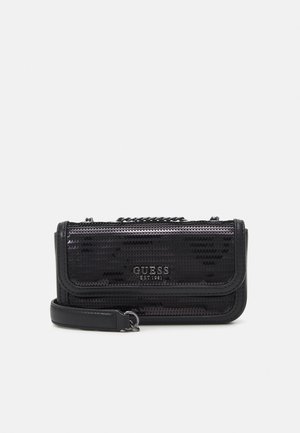 Petit sac bandoulière noir à surface texturée, rabat avant, détail de chaîne et logo "GUESS EST 1981" imprimé sur le devant.