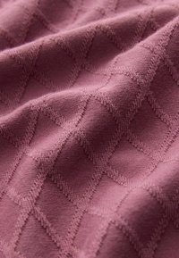 Blødt lyserødt stof med hævet diamantformet strikkemønster, der skaber en tekstureret, bølget overflade.