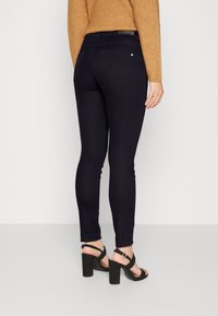 Černé skinny džíny s hladkou texturou, vybavené klasickým designem s pěti kapsami a jemnými švy, v kombinaci s černými sandály na podpatku.