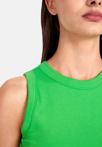 Green sleeveless top made of ribbed cotton, featuring a round neckline and stitched detailing along the collar and shoulder seams.