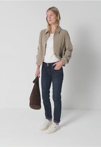 Khaki lyhyt takki puffamaisilla hihoilla, valkoinen paita, tummat farkut ja valkoiset lenkkarit. Malli pitää käsissään ruskeaa mokkasilkkikassia. Minimalistinen muotoilu.