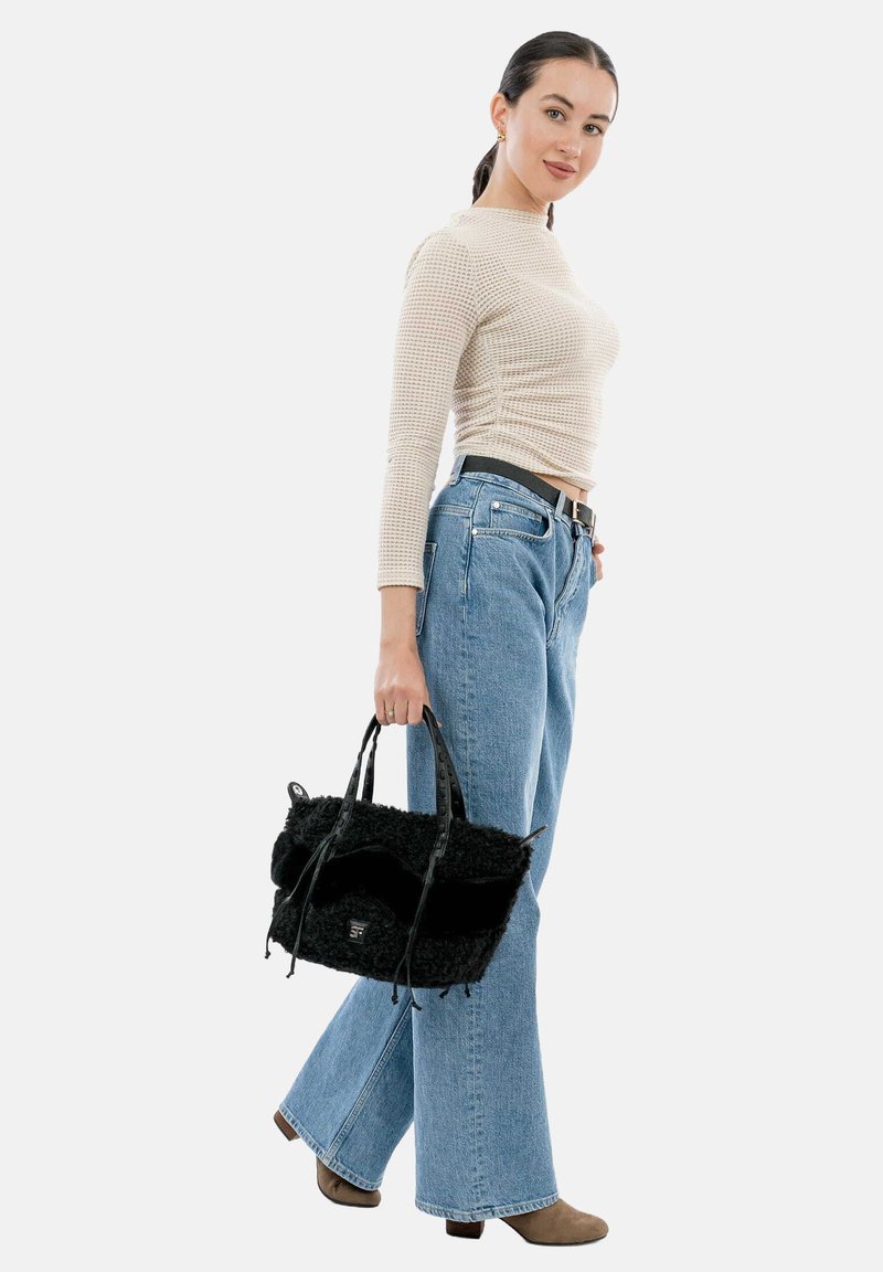 Melnā pūkainā soma ar kontrastējošām gludām siksnām, valkāta ar pieguļošu bēžu topu un gaiši ziliem platām biksēm, kas papildinātas ar melnu jostu.