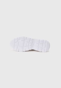 Semelle de sneaker blanche, avec une surface en caoutchouc texturé présentant des motifs variés pour une meilleure adhérence, y compris des rainures et des sections surélevées pour traction.