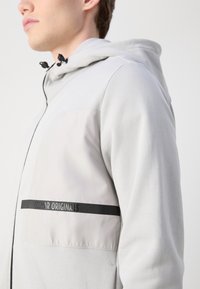 Gray hoodie with a light gray panel, black accents, adjustable hood, and a front zipper. Features "Colmar Originals" branding.