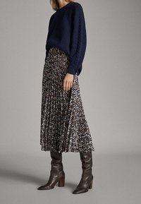 Marineblauw geribbeld sweater met lange mouwen, gecombineerd met een geplooide rok met luipaardprint tot de midi-lengte en bruine hakken, wat textuur en patroon benadrukt.