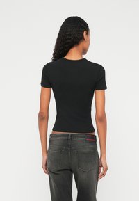 Melnas īsroku krekls ar piegulošu formu un apaļu izgriezumu, kopā ar tumši pelēniem džinsiem, kuriem uz aizmugurējā kabatas ir sarkans logo.