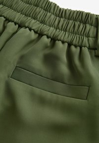 Grüstoff, strukturiert mit einem elastischen Bund und einer einzelnen Gesäßtasche. Glatte Oberfläche mit einem dezenten Glanz.