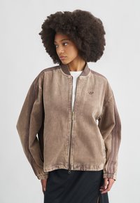 Καφέ βελούδινο μπουφάν τύπου bomber με φερμουάρ στο μπροστινό μέρος, ριμπ γιακά και φαρδιά μανίκια. Διαθέτει διακριτικό λογότυπο στο στήθος. Υφή, χαλαρή εφαρμογή.