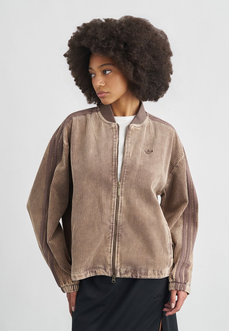 Καφέ βελούδινο μπουφάν τύπου bomber με φερμουάρ στο μπροστινό μέρος, ριμπ γιακά και φαρδιά μανίκια. Διαθέτει διακριτικό λογότυπο στο στήθος. Υφή, χαλαρή εφαρμογή.