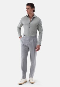 Helles graues, knopfbares Hemd mit strukturiertem Stoff, kombiniert mit hellkarierter Hose und cremefarbenen Sneakern. Gerade Silhouette, taillierte Passform.