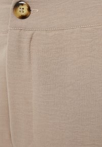 Beige fabric with a soft texture, featuring a single light brown button and stitched detailing near the pocket area.