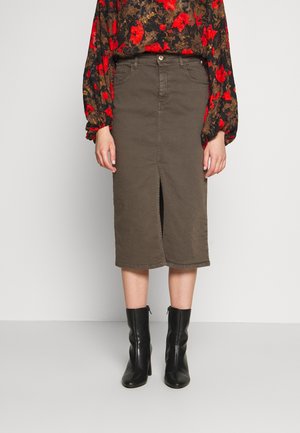 Olijfgroene denim midirok met voorin een split, vijf zakken en riemlussen, gecombineerd met een zwarte en rode bloemenblouse en zwarte laarzen met hoge hakken.