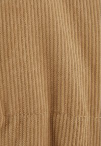 Tela de pana en un tono marrón cálido, con textura acanalada vertical y detalles de costura sutiles, creando una superficie suave y táctil.