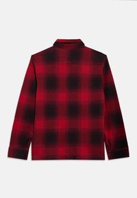 Červeno-čierna kockovaná košeľa s dlhými rukávmi a golierom, zobrazená položene plochá tak, že je vidieť zadná strana na bielom pozadí.