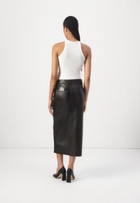 Jupe midi en cuir noir avec une texture lisse, dotée de poches arrière et d'un design ajusté. Associée à un haut sans manches blanc.