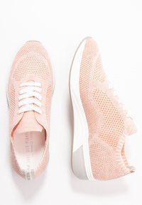 Světlé růžové prodyšné síťované tenisky s bílými tkaničkami, polstrovanou podrážkou a výraznými texturovanými vzory po celé vrchní části.