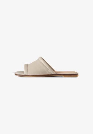 Sandale beige à bout ouvert, avec une large bride rembourrée en cuir et une semelle plate marron, vue de profil sur fond blanc.