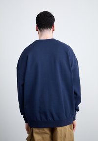 Sudadera oversized azul marino con cuello redondo, hombros caídos y puños acanalados. Textura suave, diseñada para uso casual.