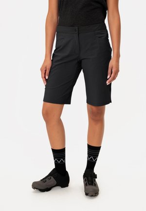 Schwarze Shorts mit glatter Textur, featuring einen Knopfverschluss, zwei vordere Taschen und eine taillierte Passform. Getragen mit grauen Mountainbikeschuhen und gestreiften Socken.