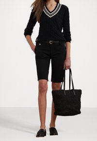 Svart kabelstickad tröja med vitrandig V-ringning, svarta skräddarsydda shorts, svart bälte och vävd svart tote-väska; ihop med loafers.