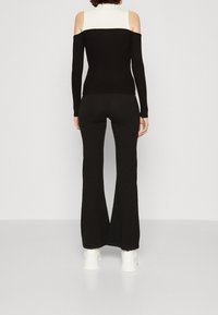 Top nero a coste con spalle scoperte e dettagli bianchi, abbinato a pantaloni neri a zampa e scarpe da ginnastica bianche, visto da dietro.