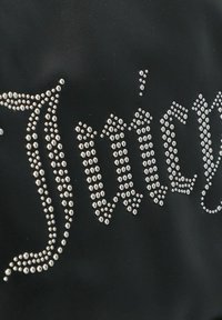 Zwart leren oppervlak met het woord "Juicy" in glanzende zilveren strass, gerangschikt in een vloeiend schrijfdesign.