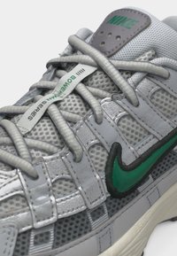 Baskets Nike grises avec un swoosh vert, tige en mesh, lacets passant par des boucles, avec le texte « Bowerman Series » sur une étiquette de lacet.
