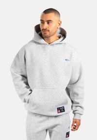 Szara bluza z kapturem z kieszenią z przodu, miękka w dotyku, niebieskie logo na klatce piersiowej oraz metka marki na dolnym brzegu. Materiał z mieszanki bawełny.