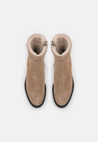 Botas de tobillo de ante beige con un forro de felpa texturizado, cierre de cremallera y suela de goma negra. La parte superior tiene un acabado suave.