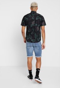 Camisetta nera a maniche corte con motivo di foglie verdi e rosa. Pantaloni shorts in denim blu chiaro con risvolti. Sneakers nere con dettagli bianchi.