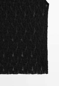 Panneau de tissu en dentelle noire avec des motifs floraux complexes et un bord sans manches, présenté sur un fond blanc.