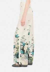 Pantaloni a gamba larga in un tessuto leggero color crema decorati con stampe floreali blu e verdi. Presentano un'alta vita e spacchi laterali.