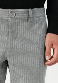 Pantalones de rayas grises hechos de una tela suave, con cierre de botón, trabillas para cinturón y costuras visibles en la cintura.